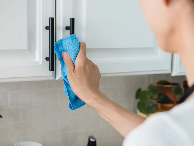 Mão a limpar os puxadores dos armários de uma cozinha